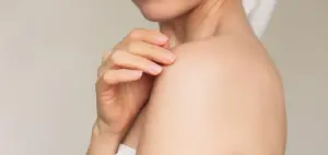 Junge Frau lächelt und berührt sanft ihre Schulter mit den Fingerspitzen