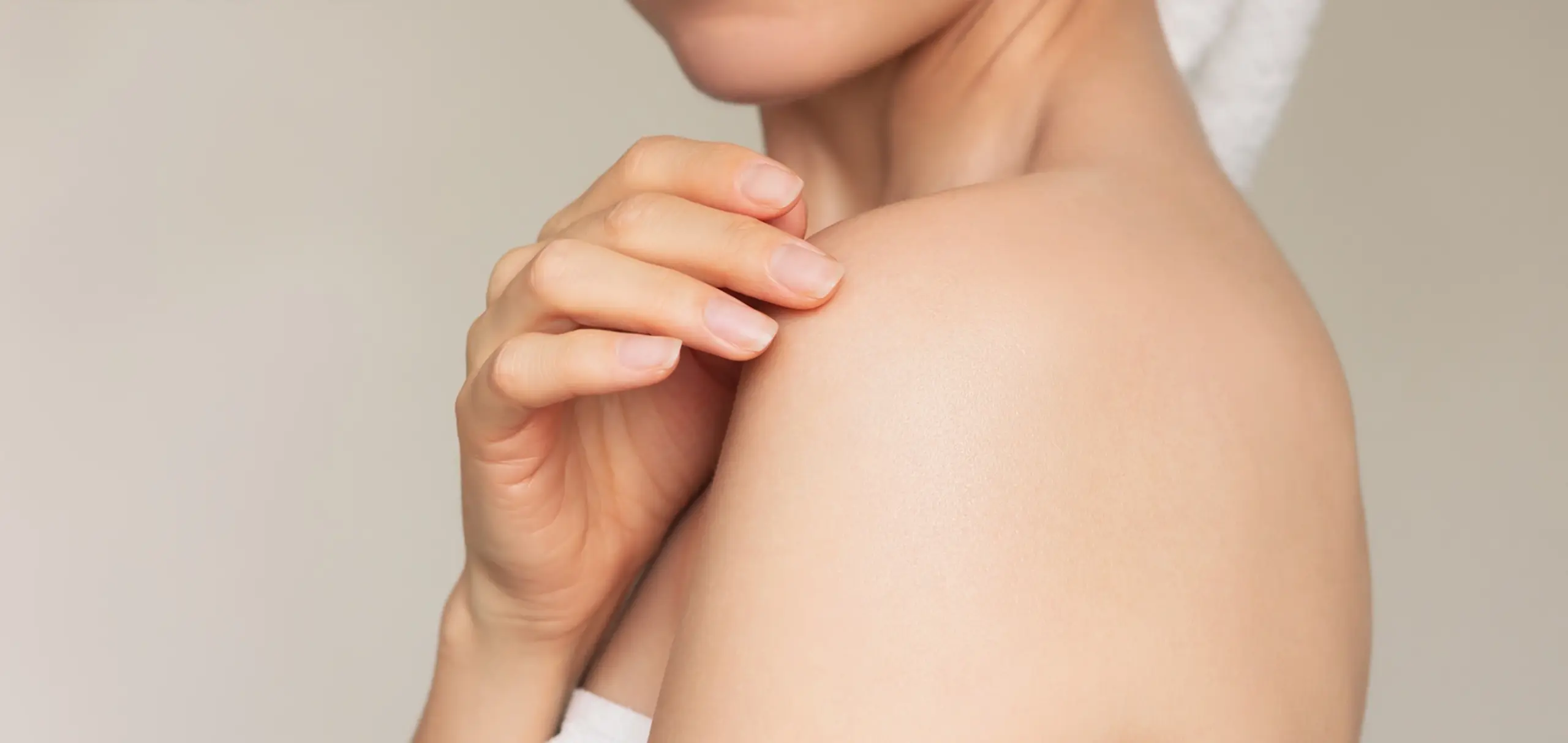 Junge Frau lächelt und berührt sanft ihre Schulter mit den Fingerspitzen