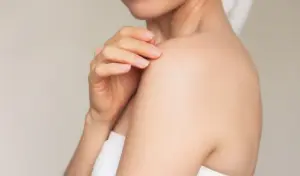 Junge Frau lächelt und berührt sanft ihre Schulter mit den Fingerspitzen